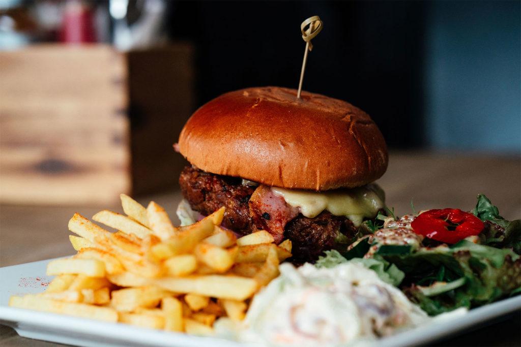 A burger with fries, coleslaw and salad on a white plate
