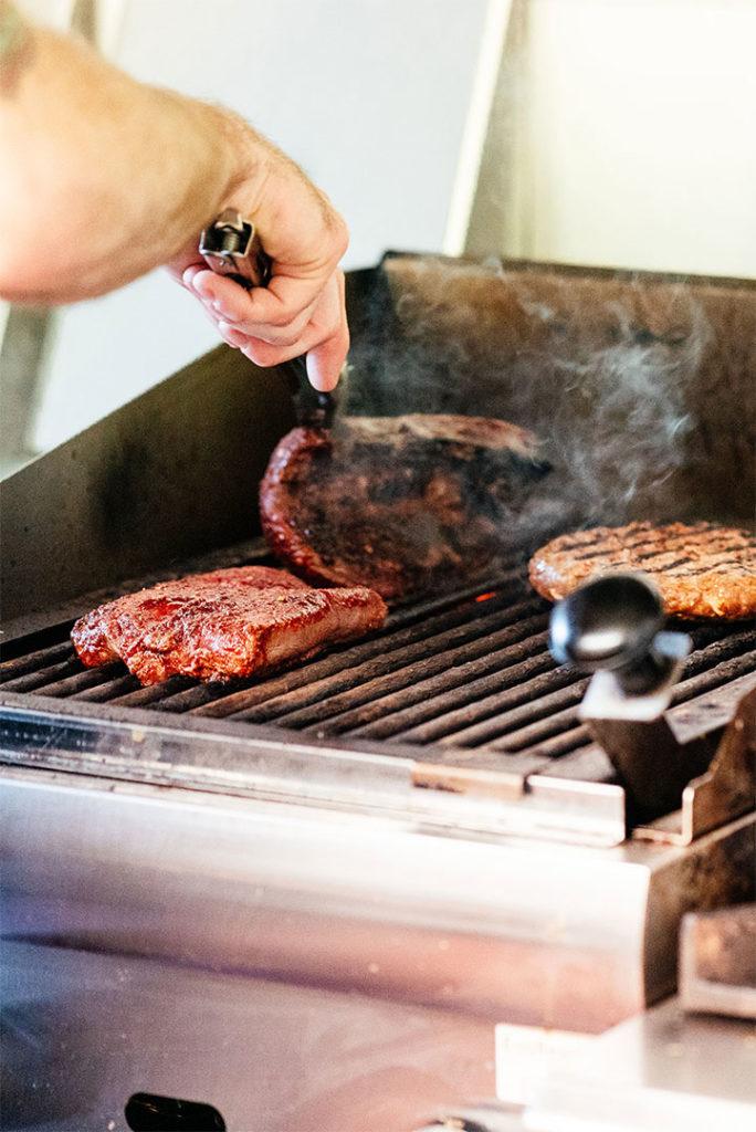 Steaks and a burger cooking on the grill