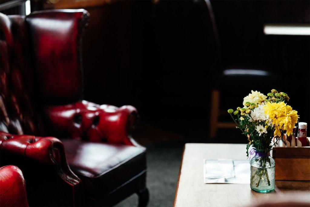 A red leather Chesterfield armchair beside a table with fresh flowers