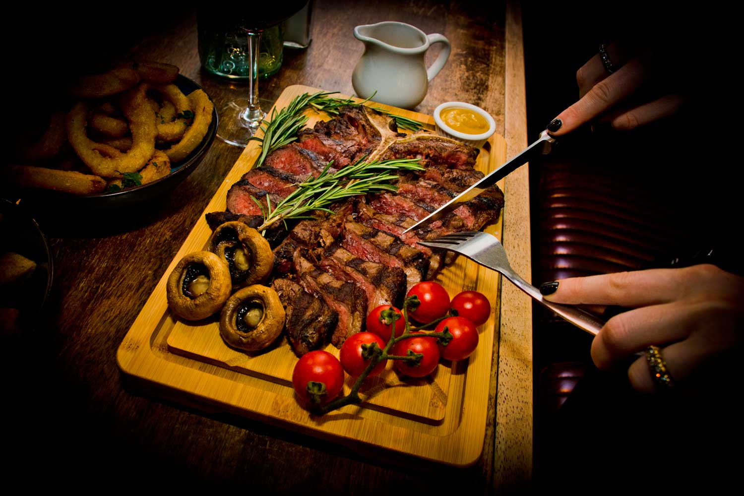 A sliced steak on a board with mushrooms and vine tomatoes