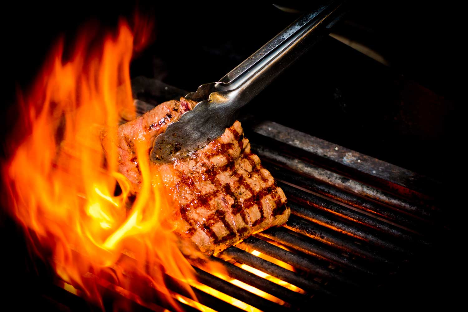 A steak searing over open flames on the grill