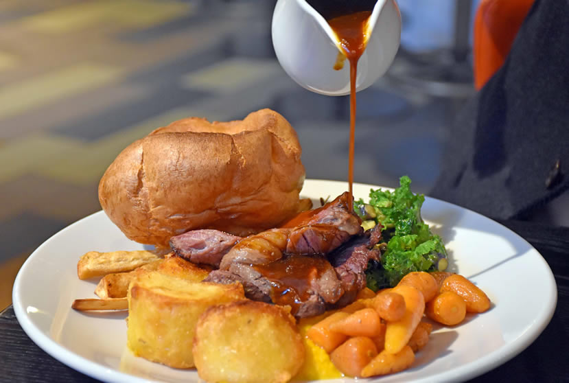 A roast beef dinner with Yorkshire pudding and gravy being poured