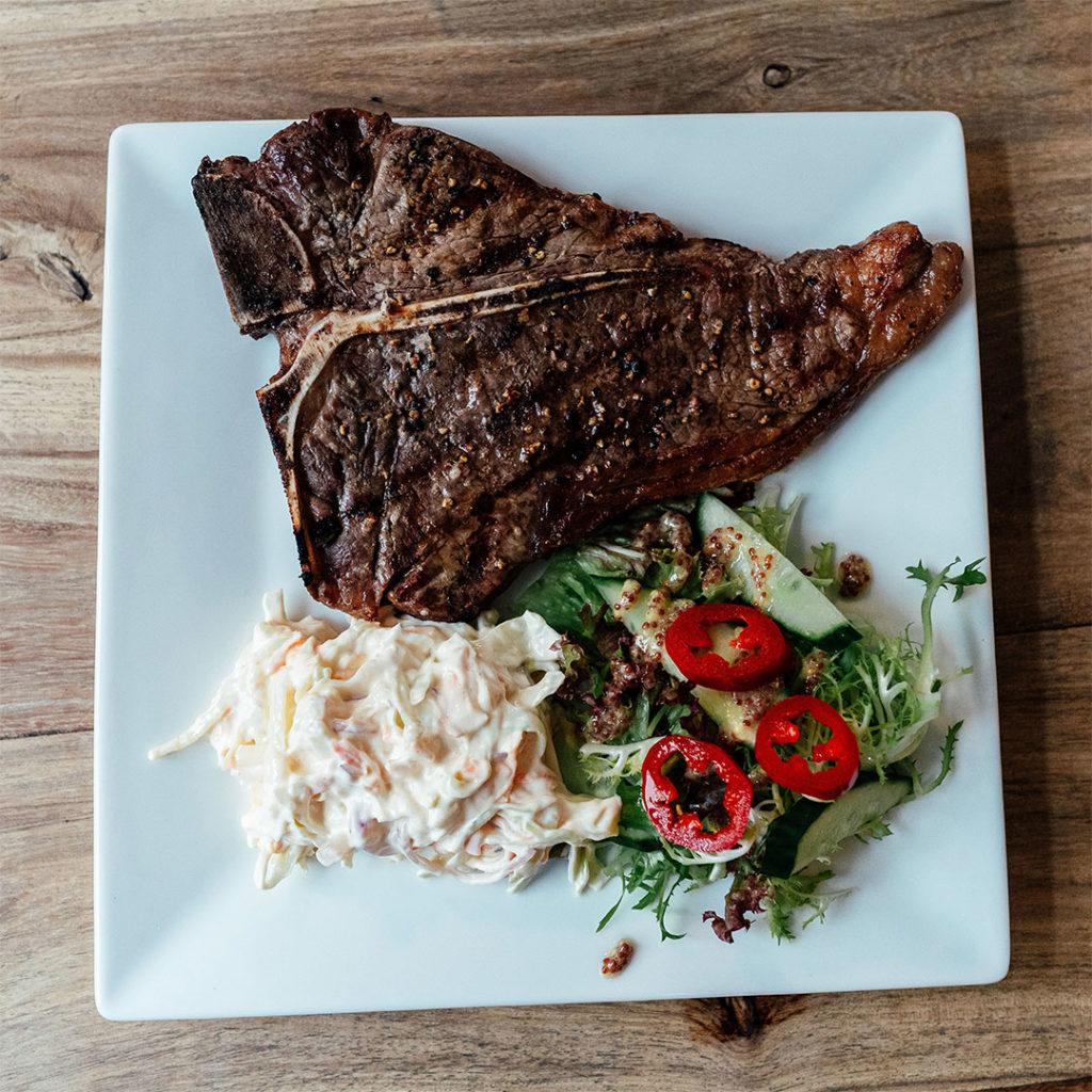 A T bone steak served with coleslaw and salad